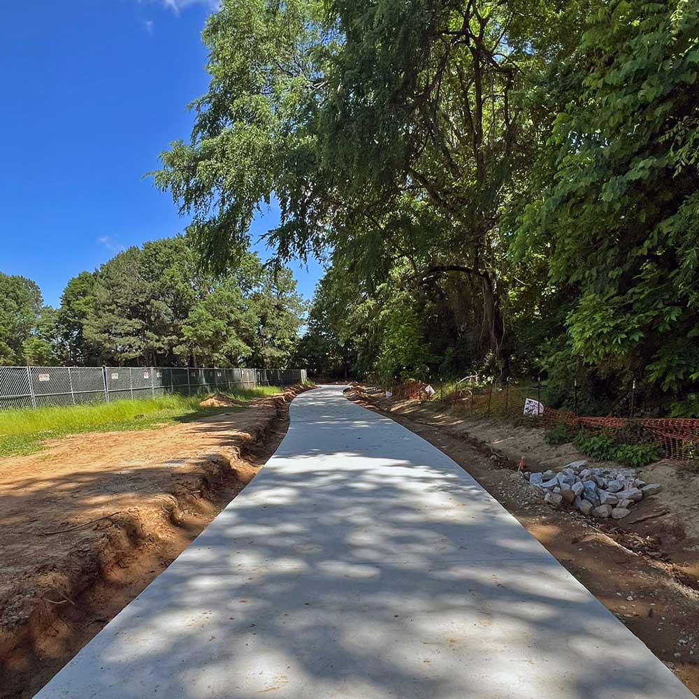 A view of the Crabtree Creek Greenway in Cary, North Carolina, featuring a wide, concrete path with trees.