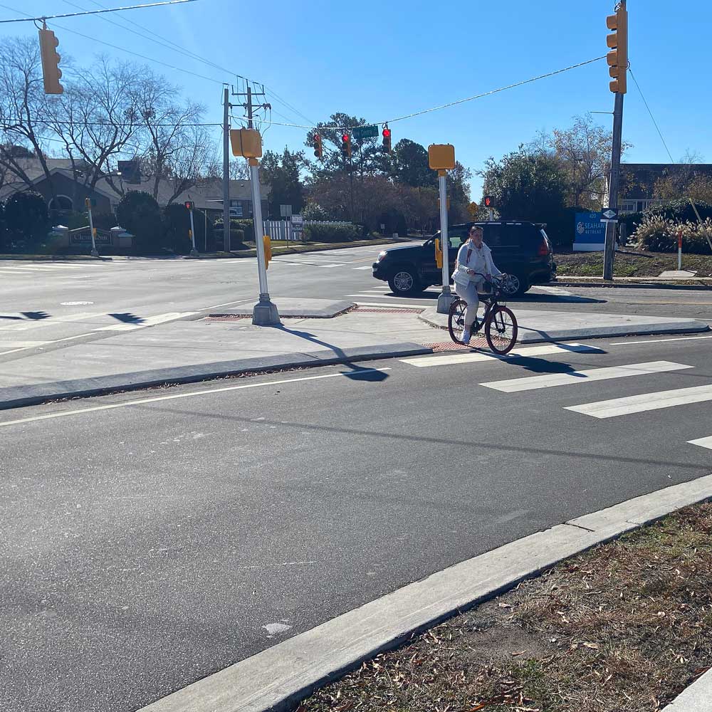 A cyclist crossing at a newly upgraded intersection with pedestrian signals and high-visibility crosswalk markings.